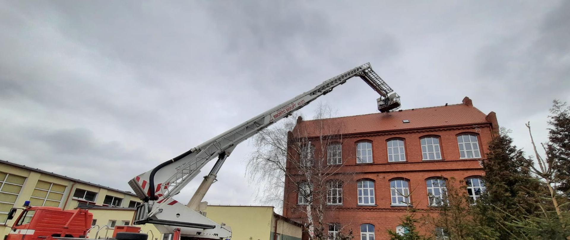 Zdjęcie wykonano w ciągu dnia, na terenie parkingu szkoły rozstawiony podnośnik straży pożarnej z koszem wystawionym nad dach szkoły Nr 1 w Sępólnie Krajeńskim. 