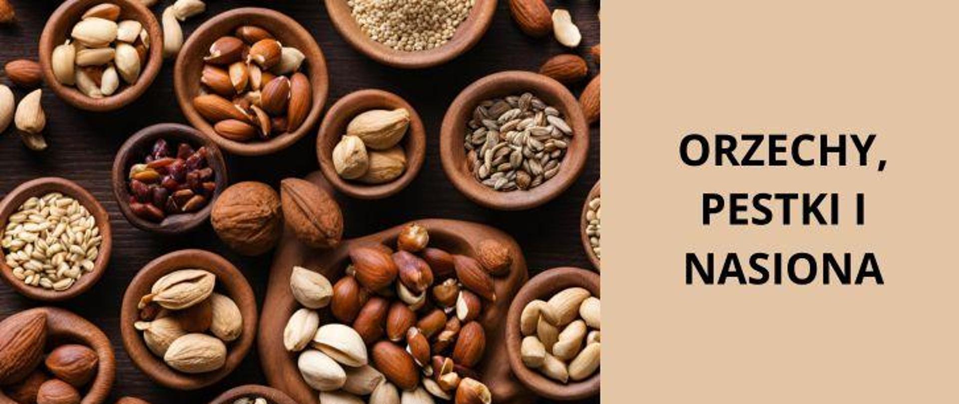 Po prawej na jasnobrązowym tle ciemny napis Orzechy, pestki i nasiona, po lewej, na ciemnym, drewnianym stole znajdują się różnej wielkości ceramiczne brązowe miski, zawierające różnego rodzaju orzechy i nasiona.