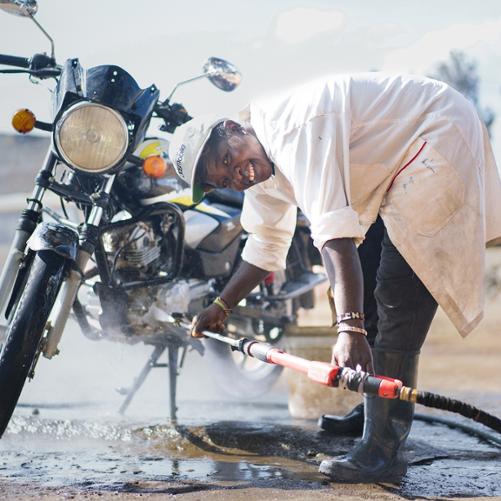 Mężczyzna myje motor woda z węża i jednocześnie uśmiecha się do kamery