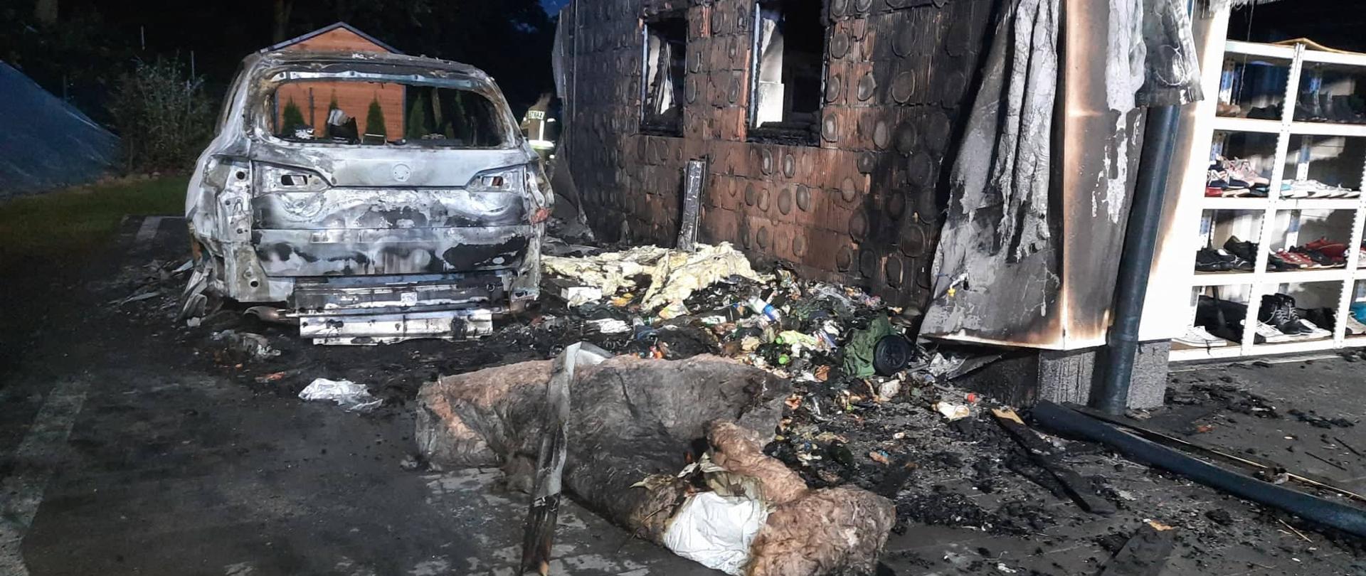 Na zdjęciu widoczny spalony samochód osobowy. Obok samochodu spalona ściana budynku - widoczna tylko ceramika ściany , całe ocieplenie spalone. Przed samochodem widoczna także wełna z poddasza i pozostałości po pożarowe.