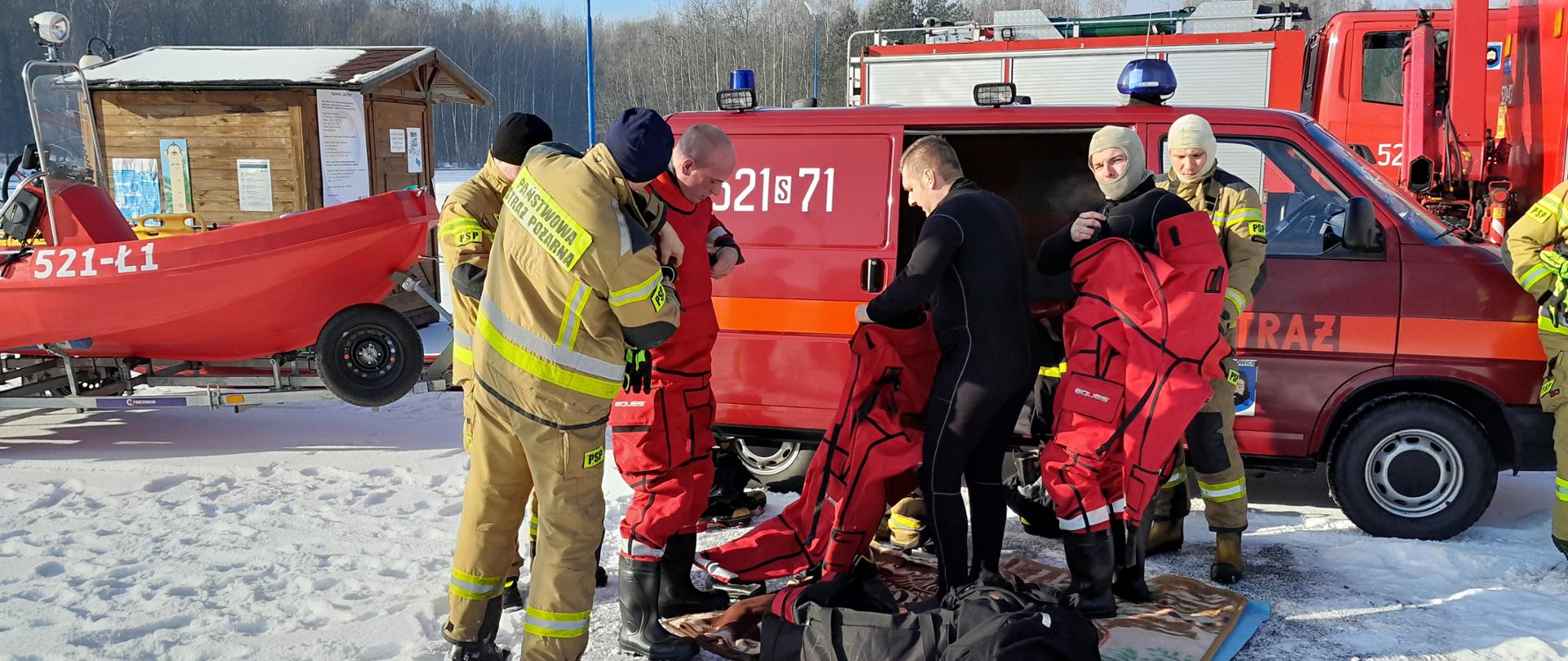 Strażacy przygotowują się do ćwiczeń ubierają się w specjalistyczne kombinezony do działań ratowniczych na akwenach wodnych. 