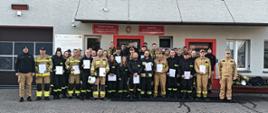 Wspólne zdjęcie strażaków OSP z zaświadczeniami po zdanym egzaminie przed budynkiem komendy