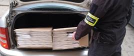 Funkcjonariusz stoi przed otwartym bagażnikiem auta, w którym są kartony z papierosami. 