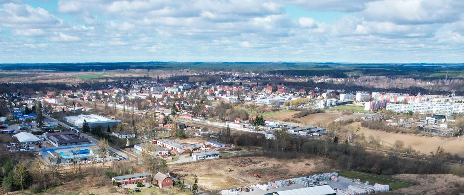Dwujezdniowa droga ekspresowa S6 widziana z góry, przebiegająca przez tereny rolnicze z polami i farmą wiatrową w tle. Nad jezdniami znajduje się bramownica z oznakowaniem kierunkowym: S6 w kierunku Szczecina oraz zjazd na drogę wojewódzką 42 w stronę Potęgowa i Skórowa.
