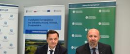 Na zdjęciu: Robert Gajda, Zastępca Prezesa Zarządu NFOŚiGW oraz Mateusz Balcerowicz, Prezes Państwowego Gospodarstwa Wodnego Wody Polskie siedzą przy stole i podpisują dokumenty.