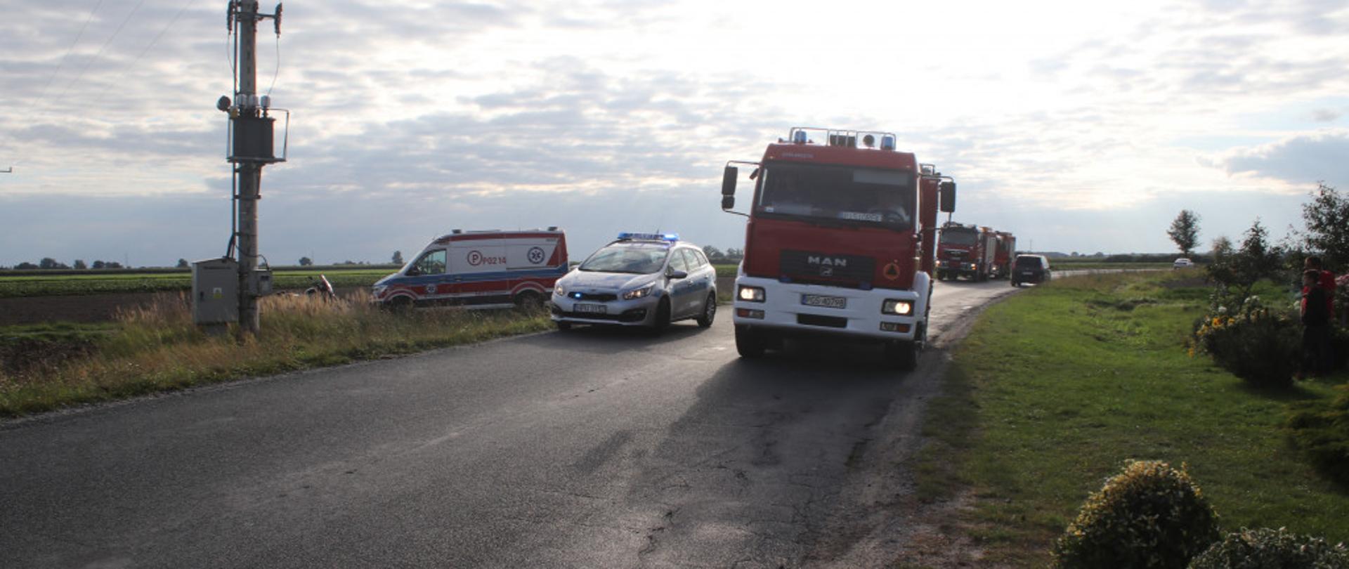 Zdjęcie przedstawia samochód pożarniczy, patrol Policji oraz karetkę pogotowia podczas działań przy wypadku.