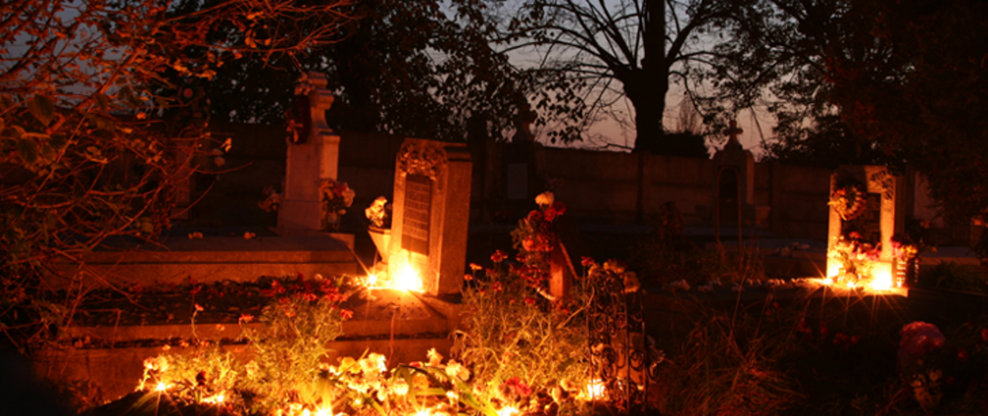 Na zdjęciu cmentarz. Jest wieczór, na grobach palą się znicze.