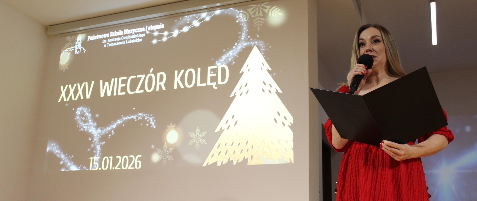 prowadząca stoi z mikrofonem w ręku i czarną teczką, zapowiada na koncercie