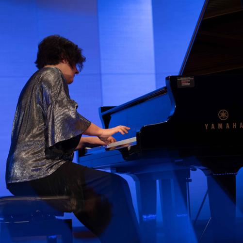 Zdjęcie przedstawia wykonawczynię koncertu podczas wykonywania utworu na fortepianie na scenie sali koncertowej, jeszcze inne ujęcie