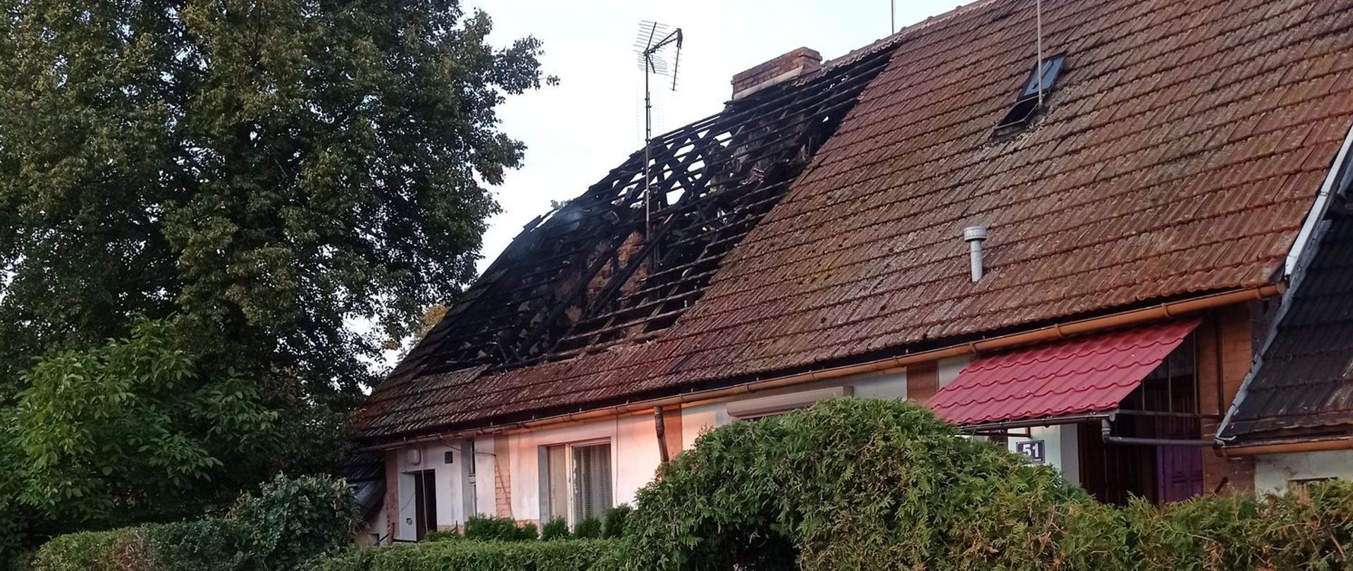 Zdjęcie przedstawia spalone poddasze w budynku wielorodzinnym.
W tle drzewa i ulica.
