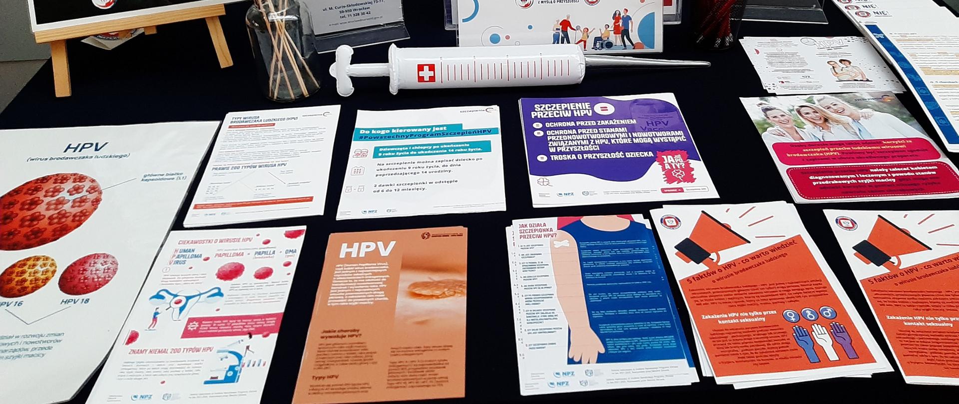 Widok stoiska edukacyjnego z rozłożonymi ulotkami dotyczącymi HPV