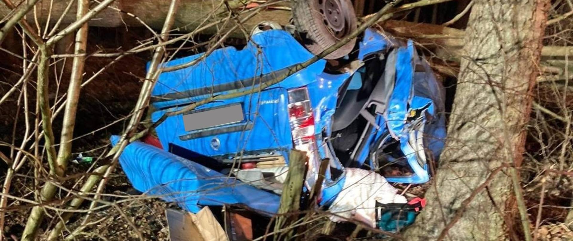 Wrak samochodu lezący na dachu między drzewami.