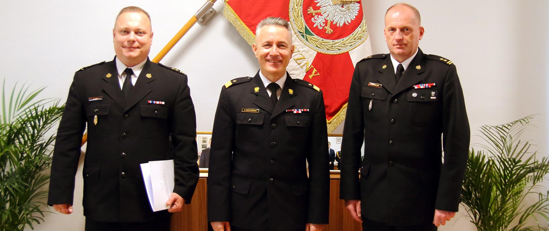 Na zdjęciu trzech wysokich rangą strażaków. W środku nadbryg. Andrzej Bartkowiak komendant główny PSP. Zdjęcie na tle sztandaru.