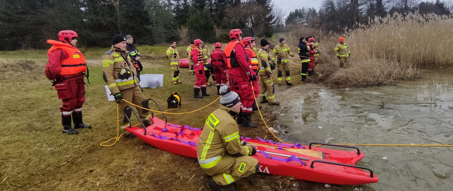 Zdjęcie przedstawia strażaków PSP i OSP w tle jezioro Głuszyńskie podczas ćwiczeń z zakresu ratownictwa lodowego.