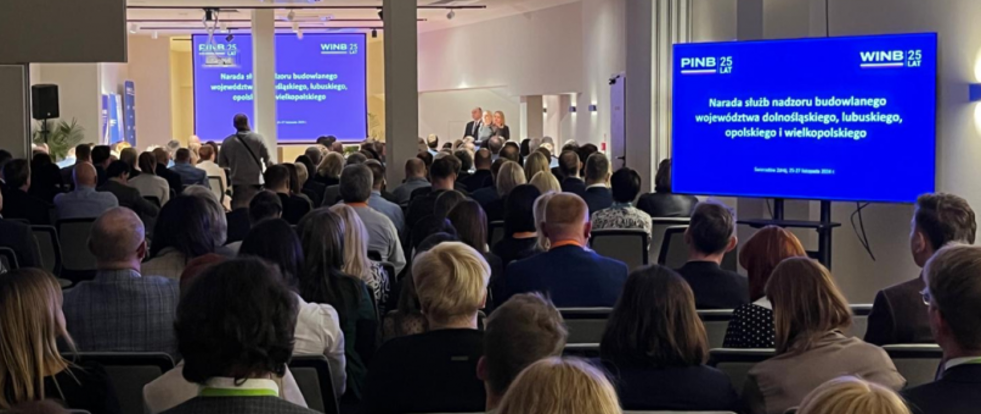 Audytorium z uczestnikami narady służb nadzoru budowlanego; na ekranach tekst o jubileuszu 25-lecia PINB i WINB oraz data i miejsce wydarzenia.