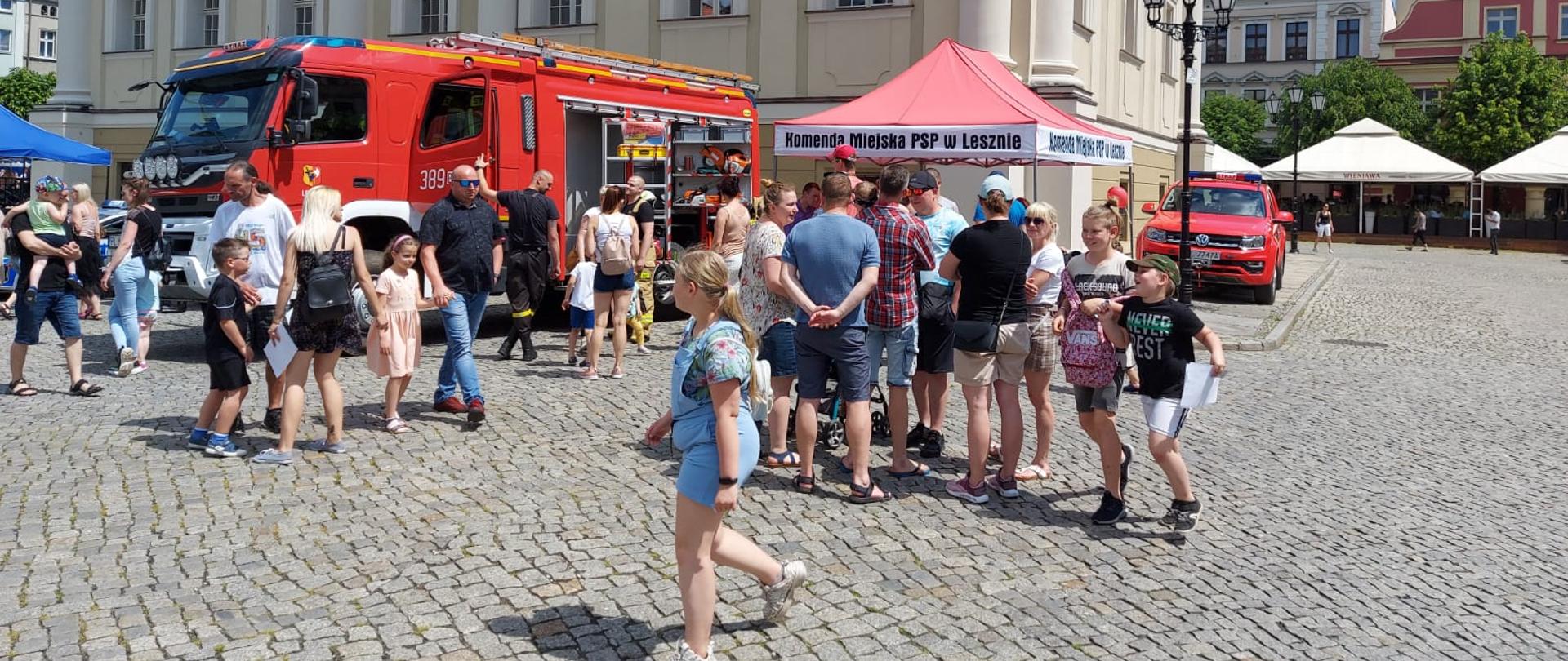 Kilkadziesiąt osób stoi przed samochodami strażackimi oraz namiotem straży pożarnej.