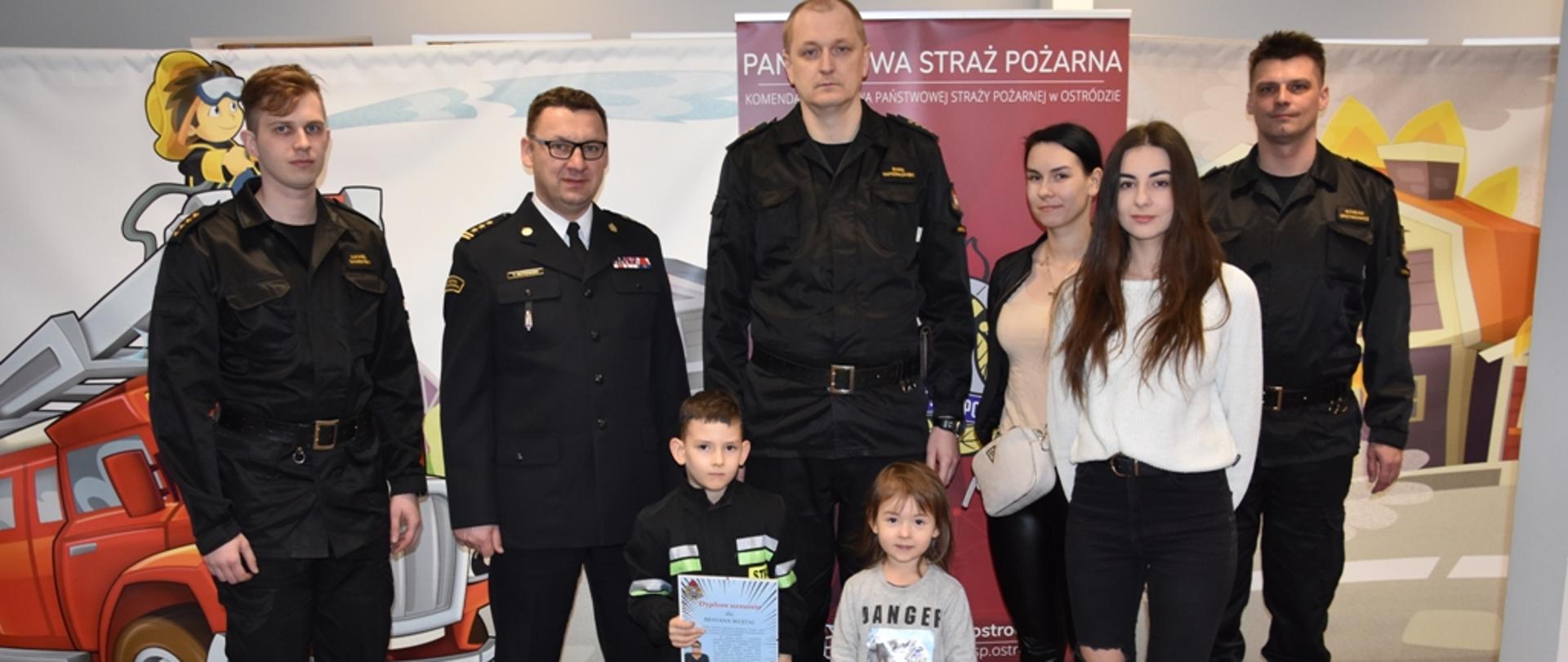 Brayan z kadrą KP PSP i rodzina stoi do pamiątkowego zdjęcia.