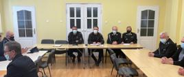 Widać strażaków siedzących przy stołach podczas spotkania