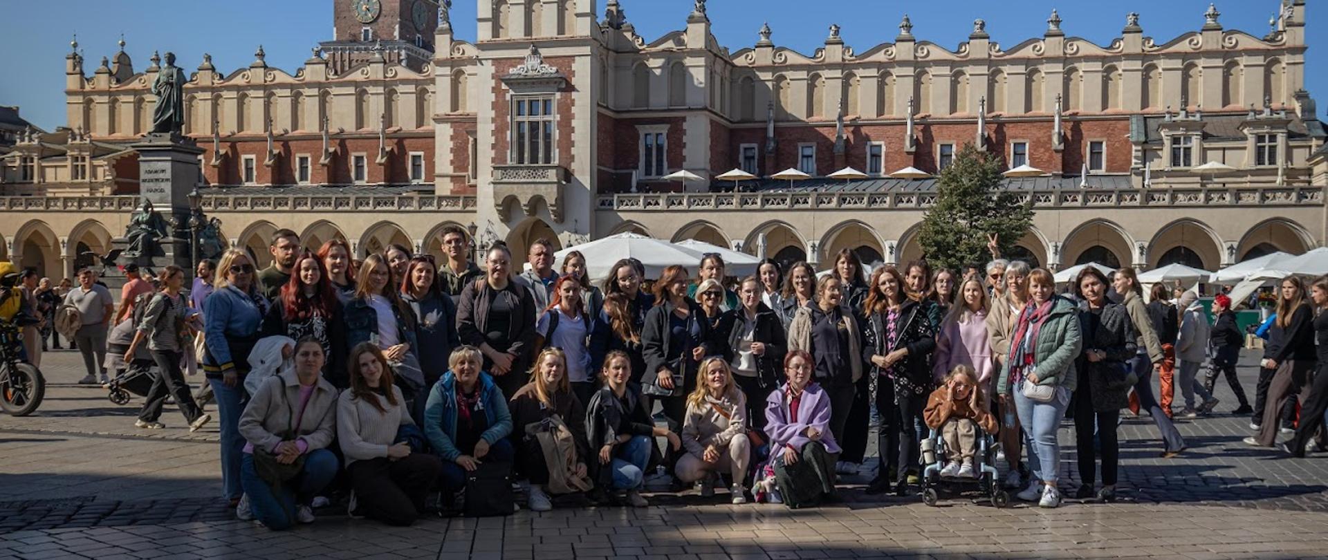 Na krakowskim rynku pozuje grupa słuchaczy oraz nauczycieli Studium . W tle zabytkowe budynki Sukiennic i wieża Kościoła Mariackiego.