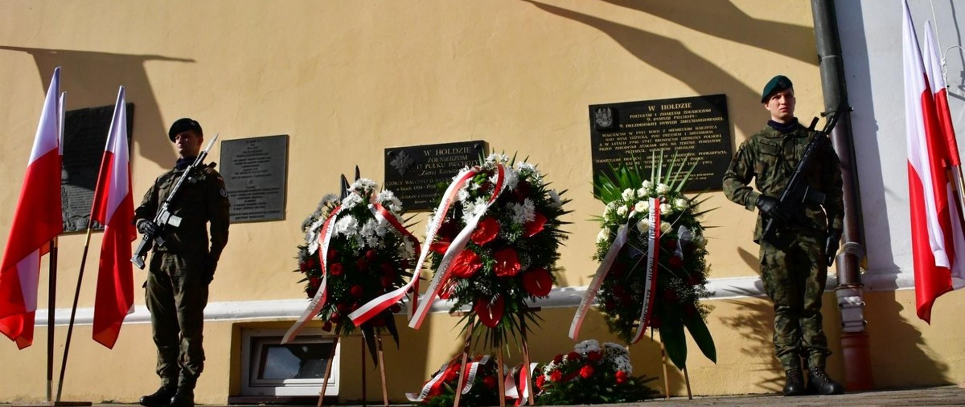 Uroczysta warta. Wieńce i wiązanki kwiatów pod tablicami umieszczonymi na ścianie Kościoła