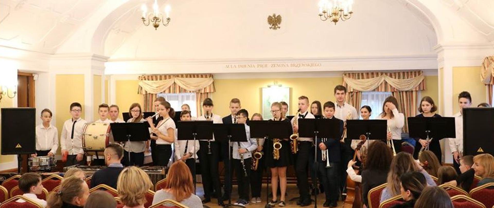 zdjęcie przedstawia orkiestrę szkolną na scenie w auli