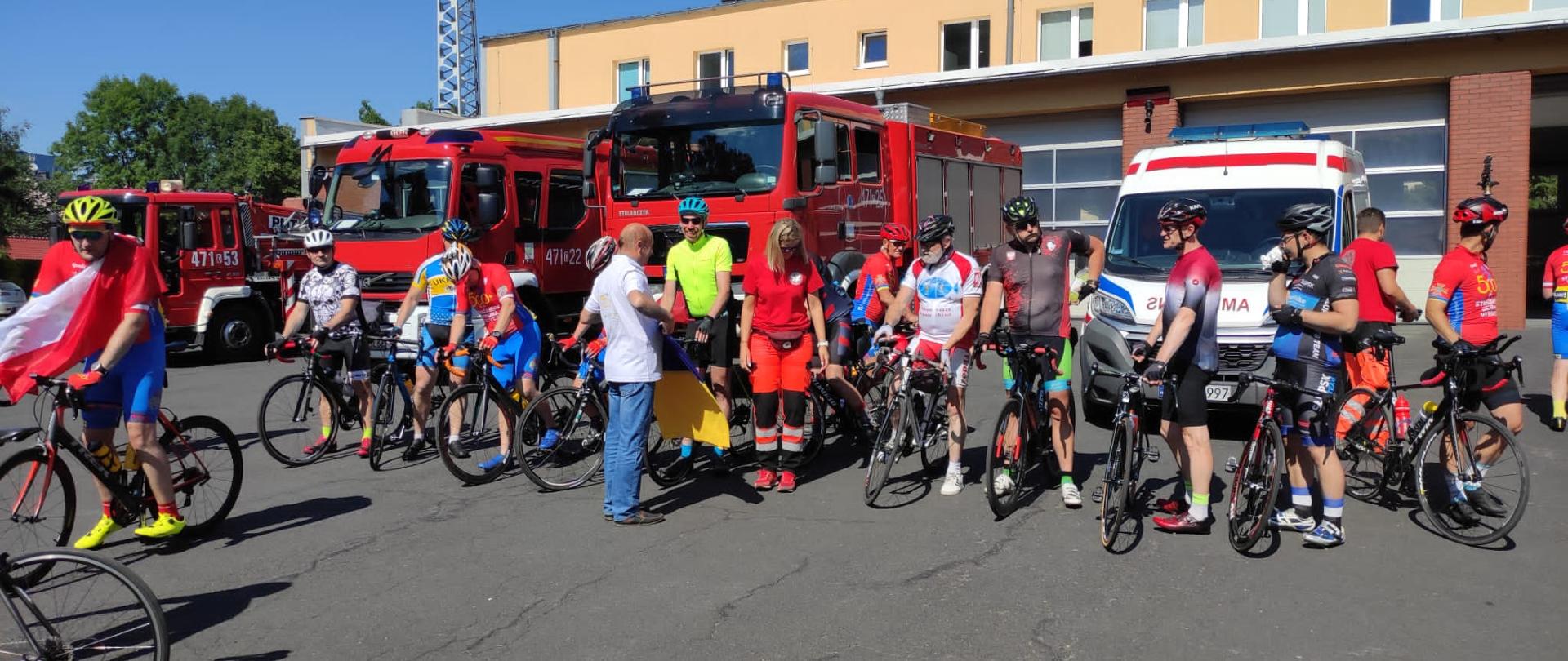Uczestnicy ultramaratonu na placu wewnętrznym KP PSP w Oleśnie. Zdjęcie przed samochodami pożarniczymi oraz ambulansem.