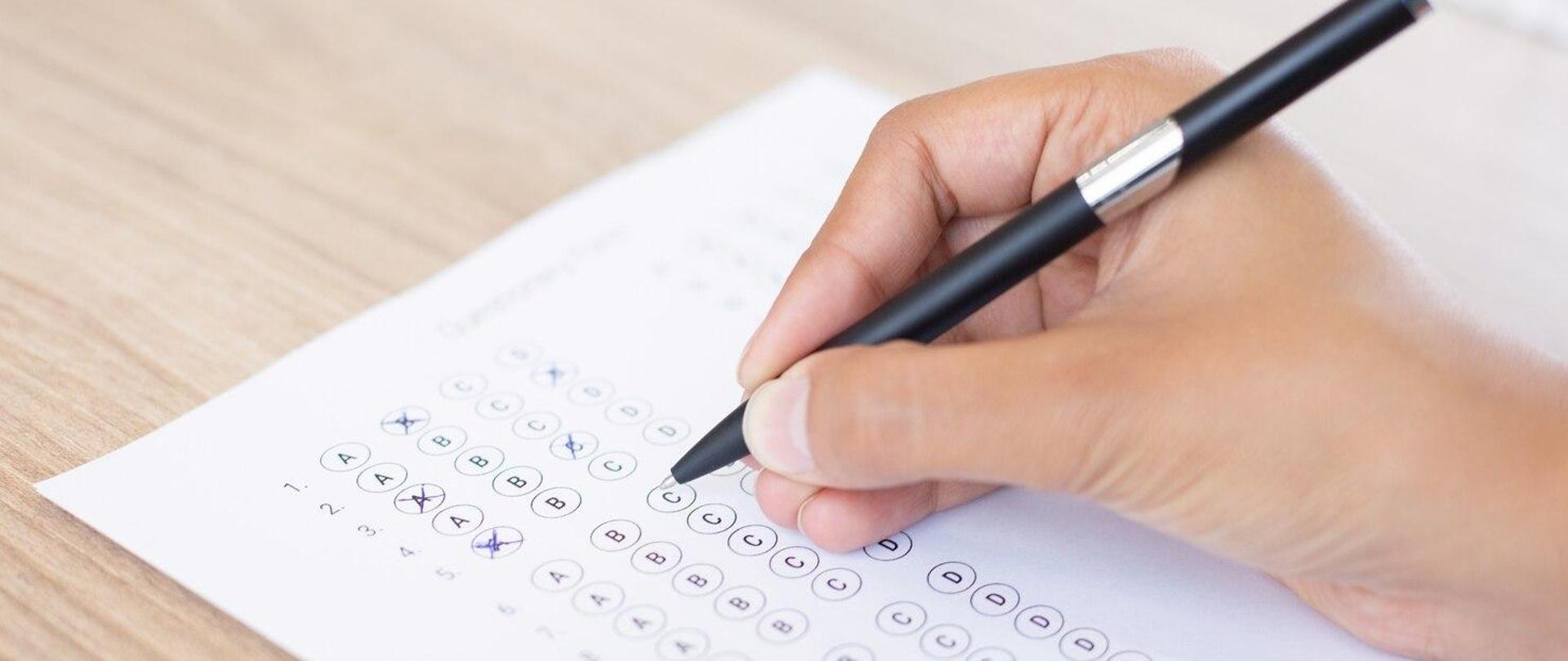 Na zdjęciu karta testowa i dłoń, która trzyma długopis. 