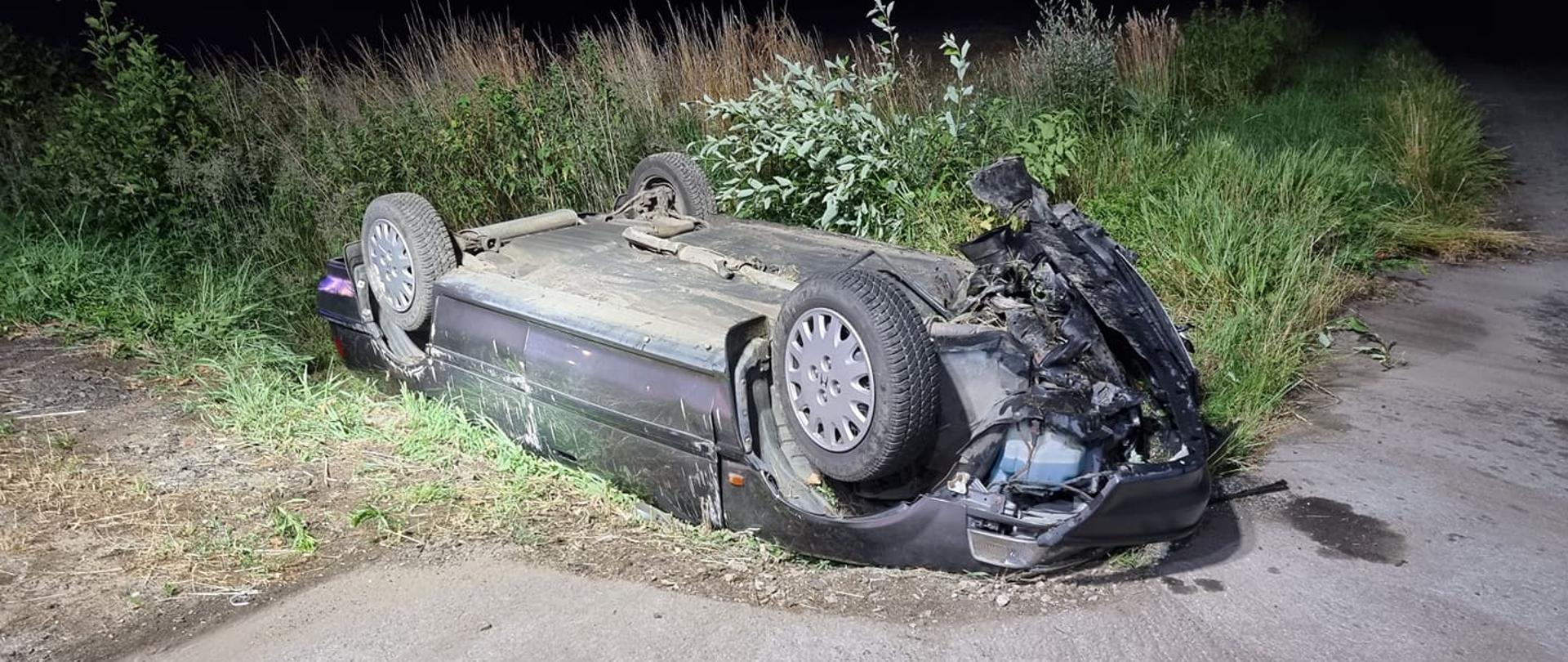 Uszkodzony samochód leży na drodze do góry podwoziem
