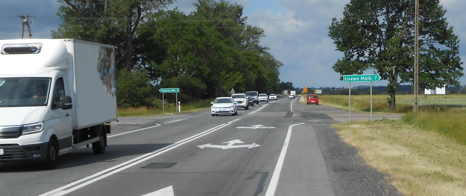 Zdjęcie przedstawia skrzyżowanie drogi krajowej nr 22 w Kończewicach. Na pierwszym planie droga z jadącymi samochodami.
