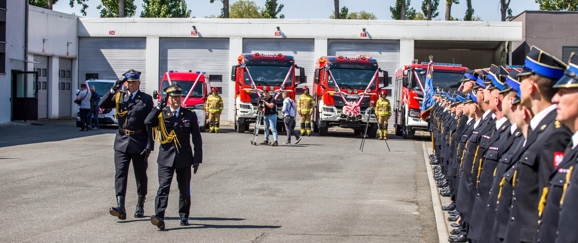 Komendant Główny PSP gen. bryg. Andrzej Bartkowiak wraz z dowódcą uroczystości (oboje w mundurach galowych) dokonują przeglądu pododdziałów na uroczystości wojewódzkiego Dnia Strażaka województwa opolskiego. Po prawej stronie strażacy PSP w mundurach galowych. W tle samochody pożarnicze.