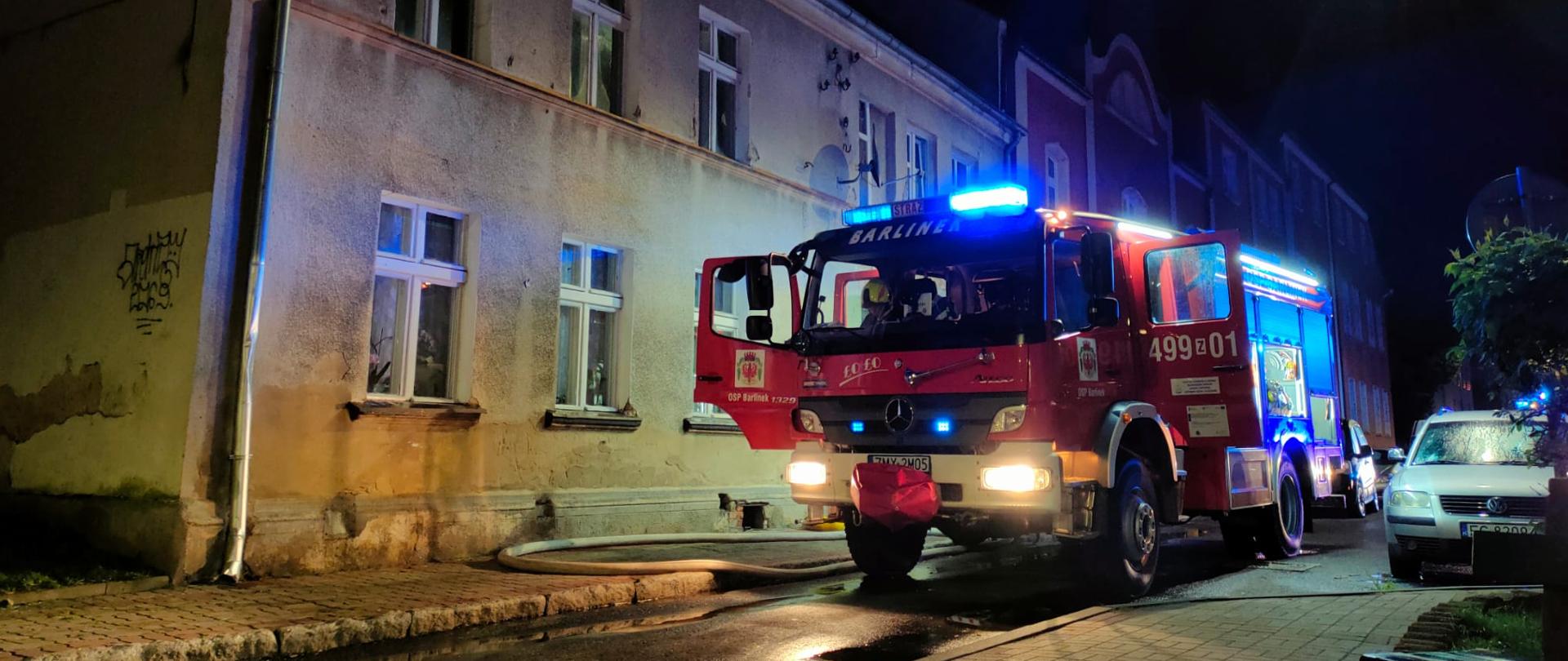 Na zdjęciu widać pojazd gaśniczy oraz budynek wielorodzinny w tle.