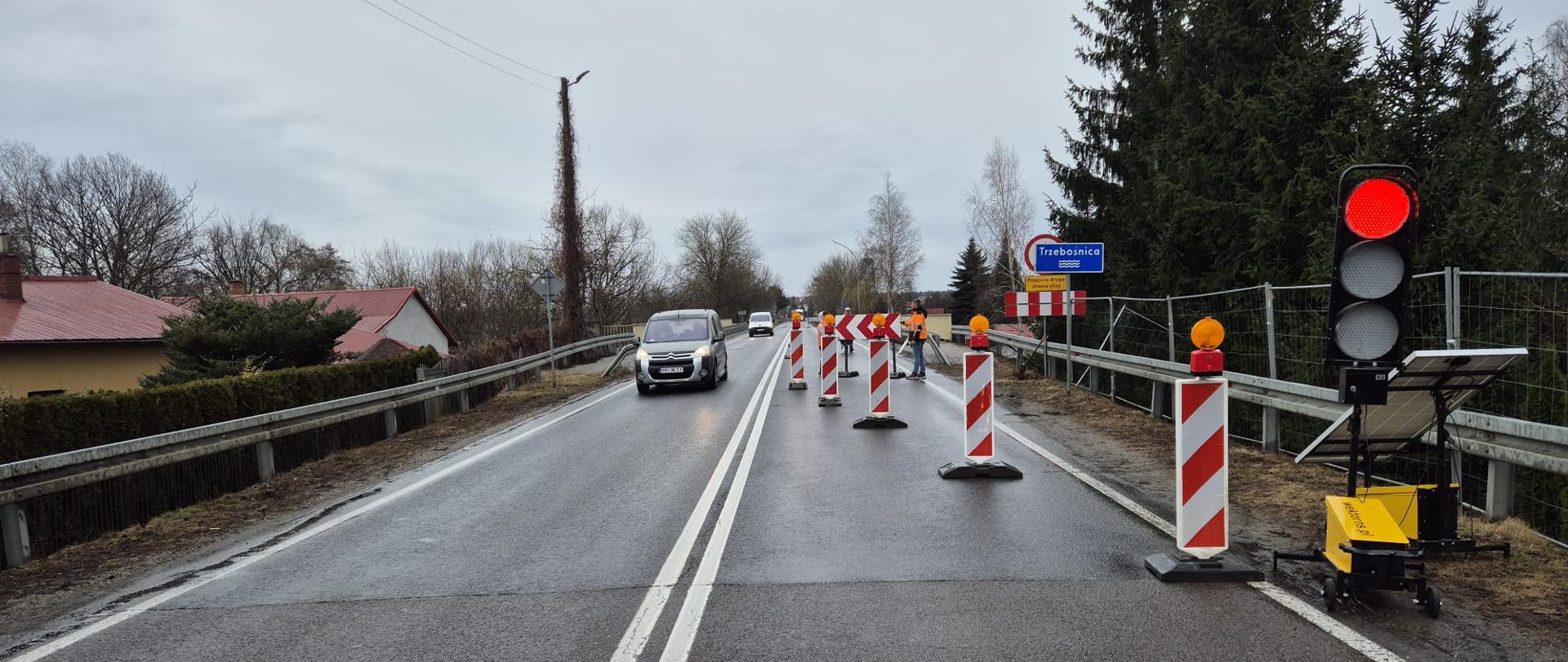 Na zdjęciu widać sygnalizację świetlną i wygrodzony jeden pas drogi krajowej nr 77. Po lewej stronie widać jadący samochód. Na sygnalizatorze świeci się czerwone światło. 