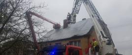 Widać samochód strażacki, za nim budynek mieszkalny, strażacy zabezpieczają uszkodzony dach plandeką