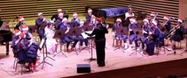 Grająca orkiestra dęta z dyrygentką na scenie sali koncertowej PSM