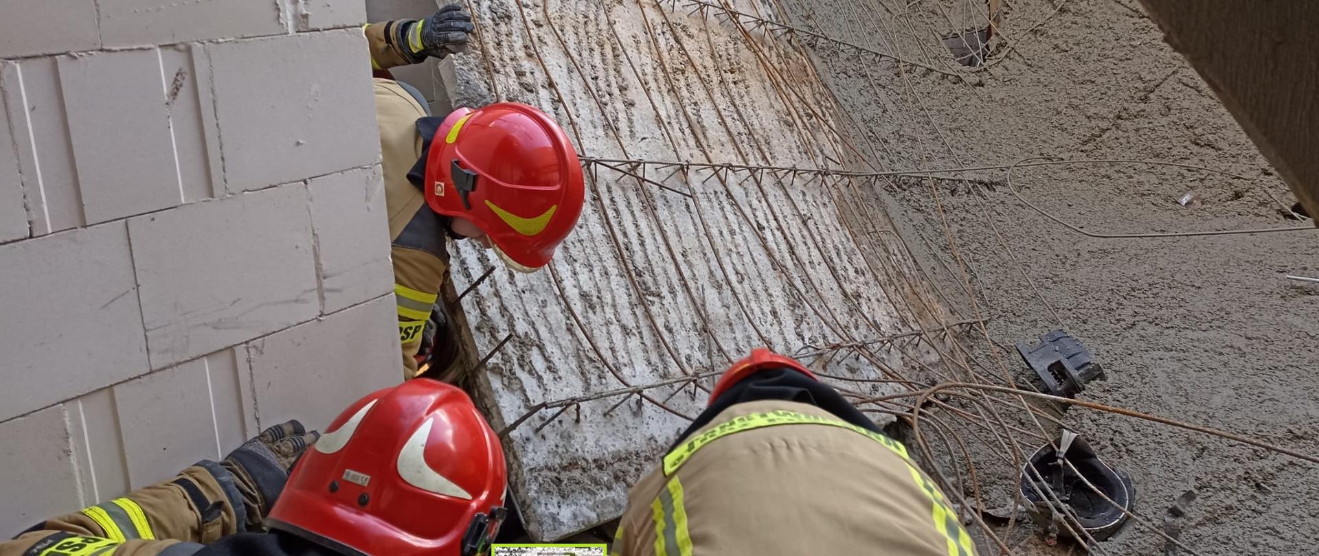 Strażacy wykonują dostęp do poszkodowanego mężczyzny, który jest przygnieciony szalunkiem. 