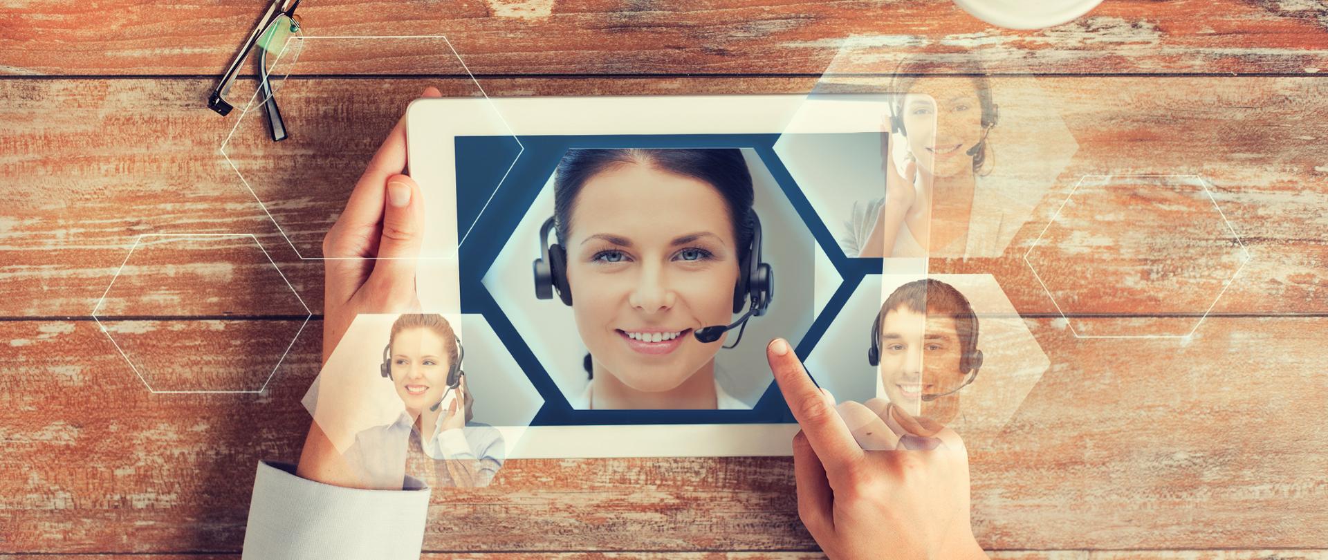 Tablet z widokiem uśmiechniętej kobiety ze słuchawkami i mikrofonem na tle stołu 