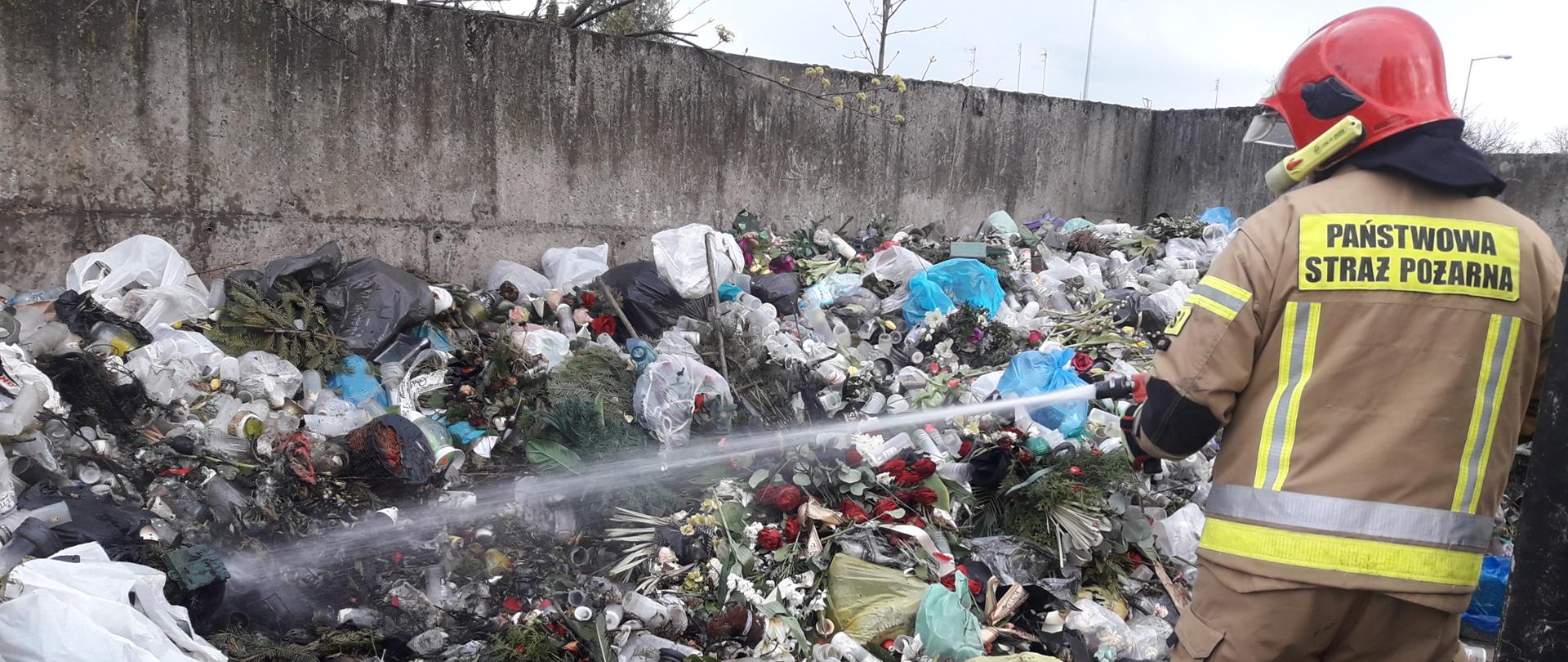 Sterta śmieci, po prawej stronie strażak który je gasi.