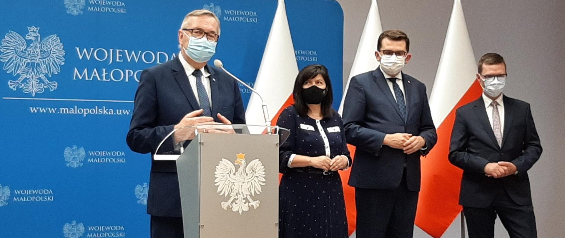 Zdjęcie zbiorowe. Na pierwszym planie minister Szwed stojący przy mównicy, na której widoczne jest godło Polski. W tle stojące dwie flagi narodowe.