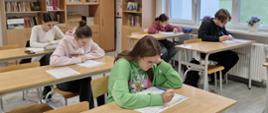 Uczniowie siedzący w szkolnych ławkach rozwiązują test.