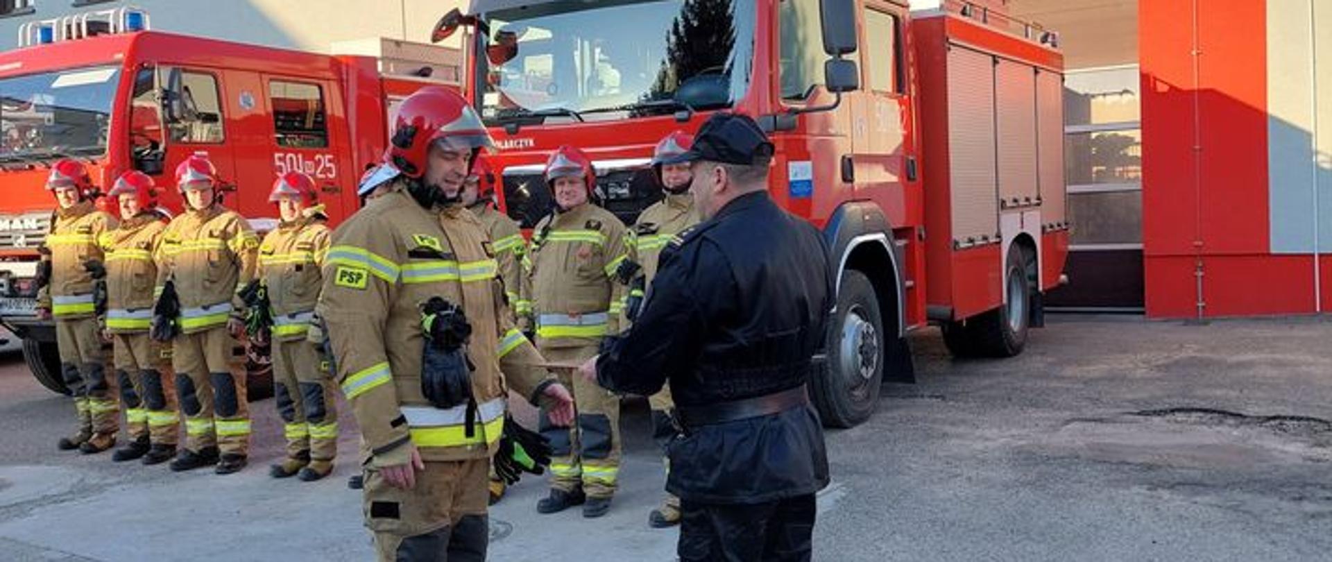 Strażak odbiera z rąk komendanta wyróżnienie za bohaterską postawę podczas akcji.