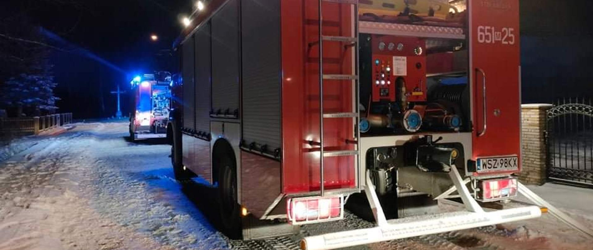 Fotografia przedstawiająca dwa pojazdy pożarnicze z rozwiniętymi wężami podczas zdarzenia wybuchu gazu w domu jednorodzinnym