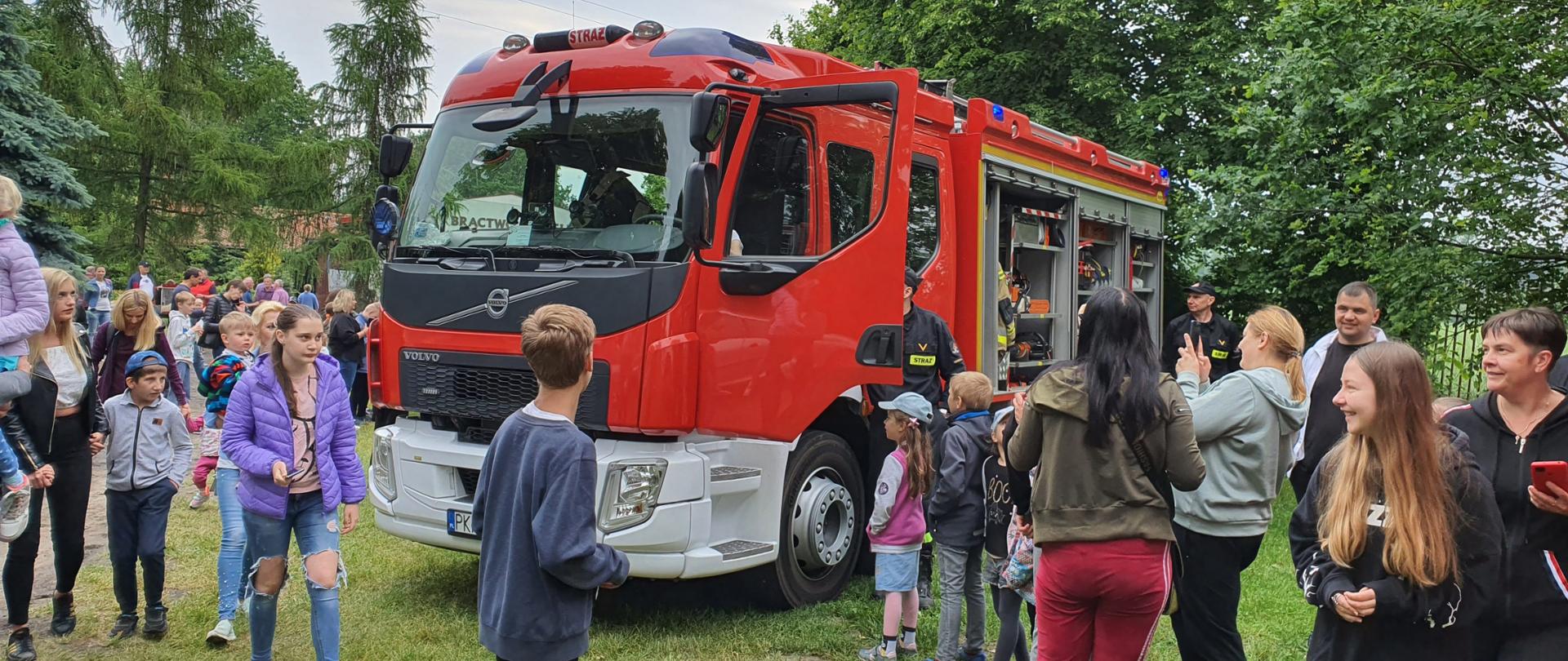 Na strzelnicy bractwa kurkowego stoją wozy pożarnicze. Wokół pojazdów dzieci podziwiają sprzęt strażacki. Trwają pokazy. Każdy z dzieci wsiada do pojazdu oraz korzysta z możliwości spotkania ze strażakami