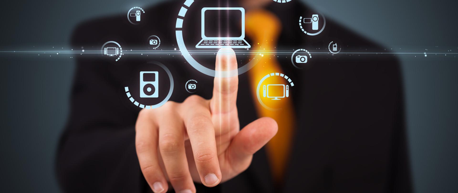 Męska dłoń z palcem skierowanym na laptop.