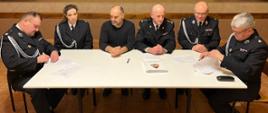 Sześcioro ludzi siedzi przy stole, podpisując dokumenty porozumienia, w sprawie włączenia jednostki OSP Rumian do Krajowego Systemu Ratowniczo- Gaśniczego.
