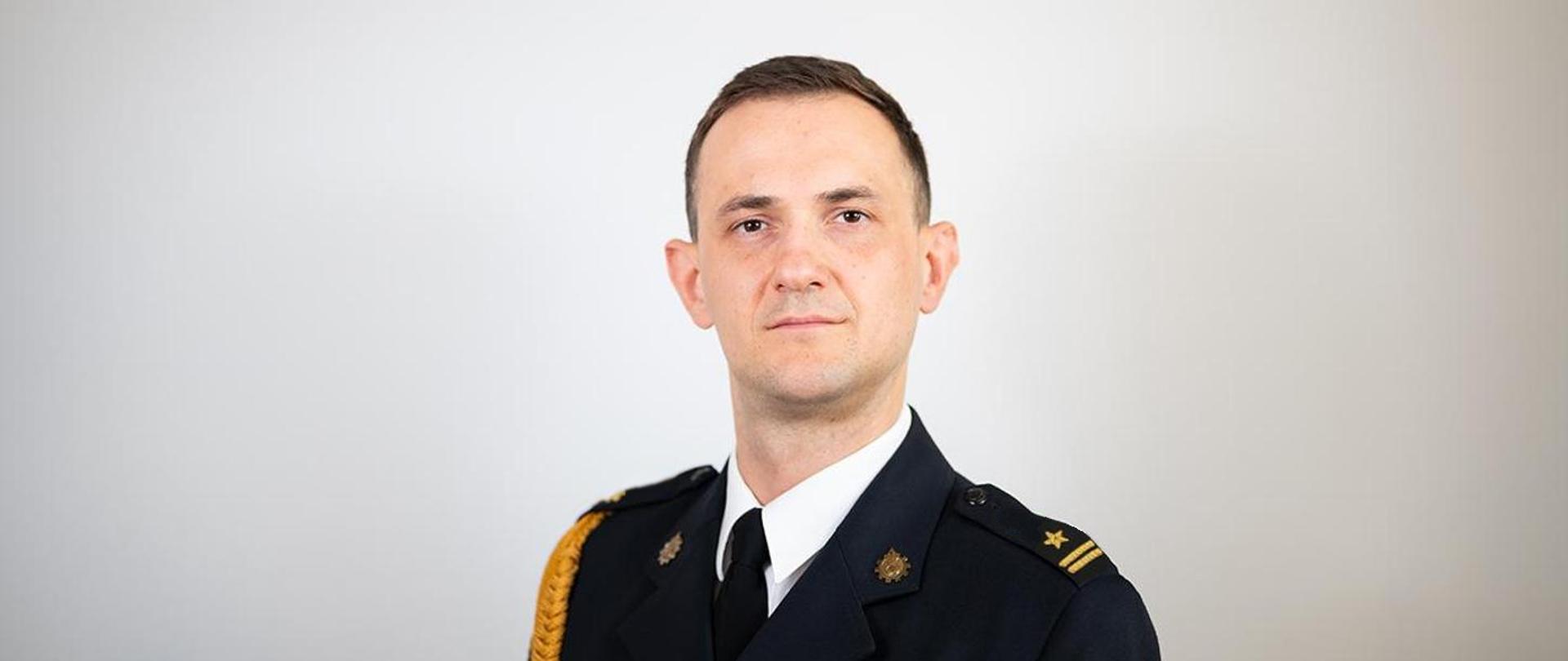 Mężczyzna, w mundurze wyjściowym Państwowej Straży Pożarnej w stopniu młodszego brygadiera.