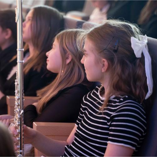 Zdjęcie przedstawia małą flecistkę zasiadającą na widowni w sali koncertowej ZPSM