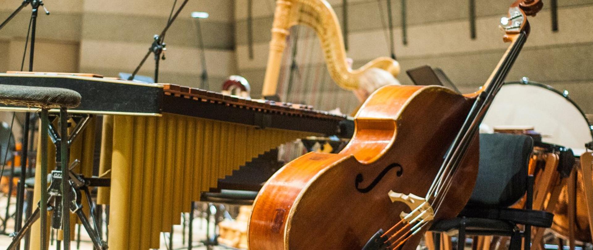 zdjęcie - instrumenty muzyczne w sali prób; na pierwszym planie kontrabas oparty o krzesło i obok niego marimba; na dalszym planie inne instrumenty