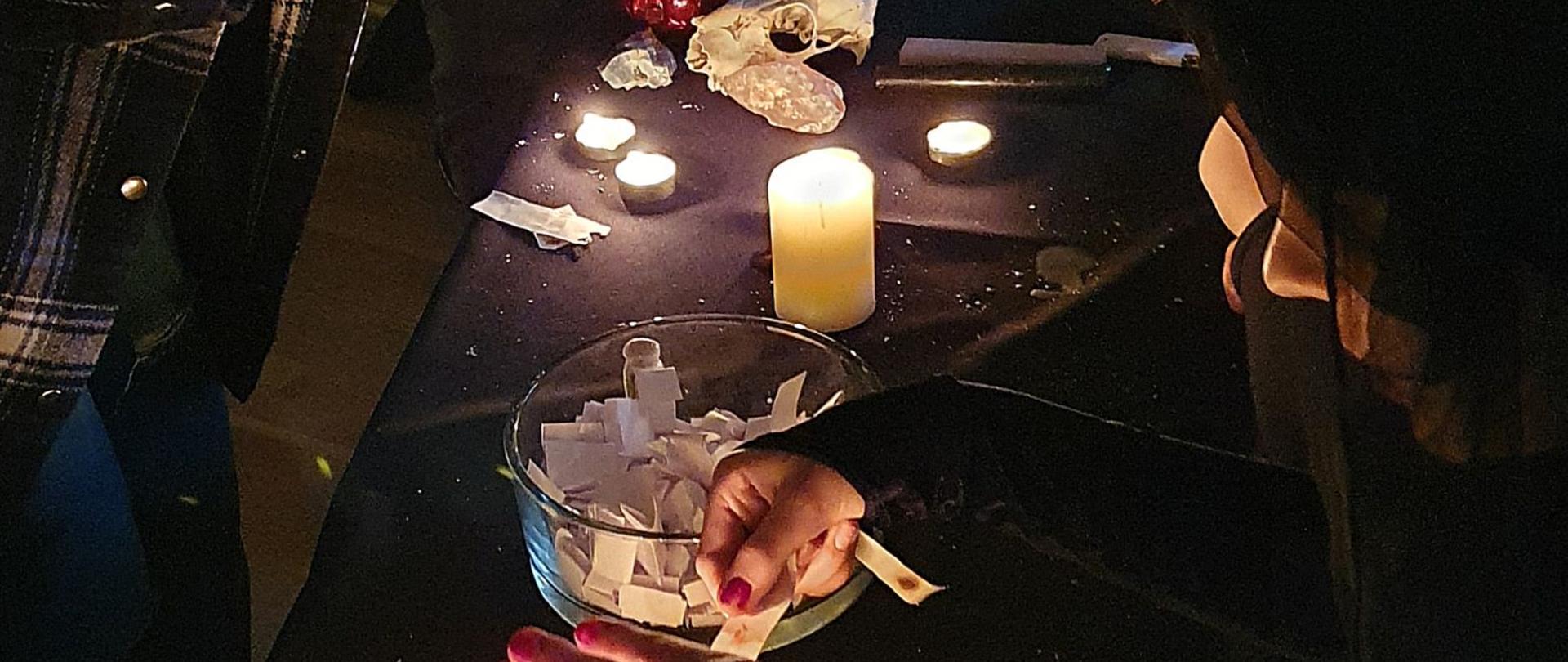 Zdjęcie - w centrum stół, na nim zapalone świece, naczynie z losami. Wokoło uczniowie.