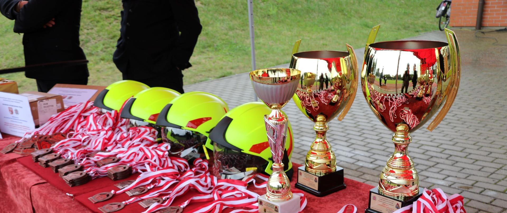 Na zdjęciu widać medale, puchary oraz hełmy strażackie