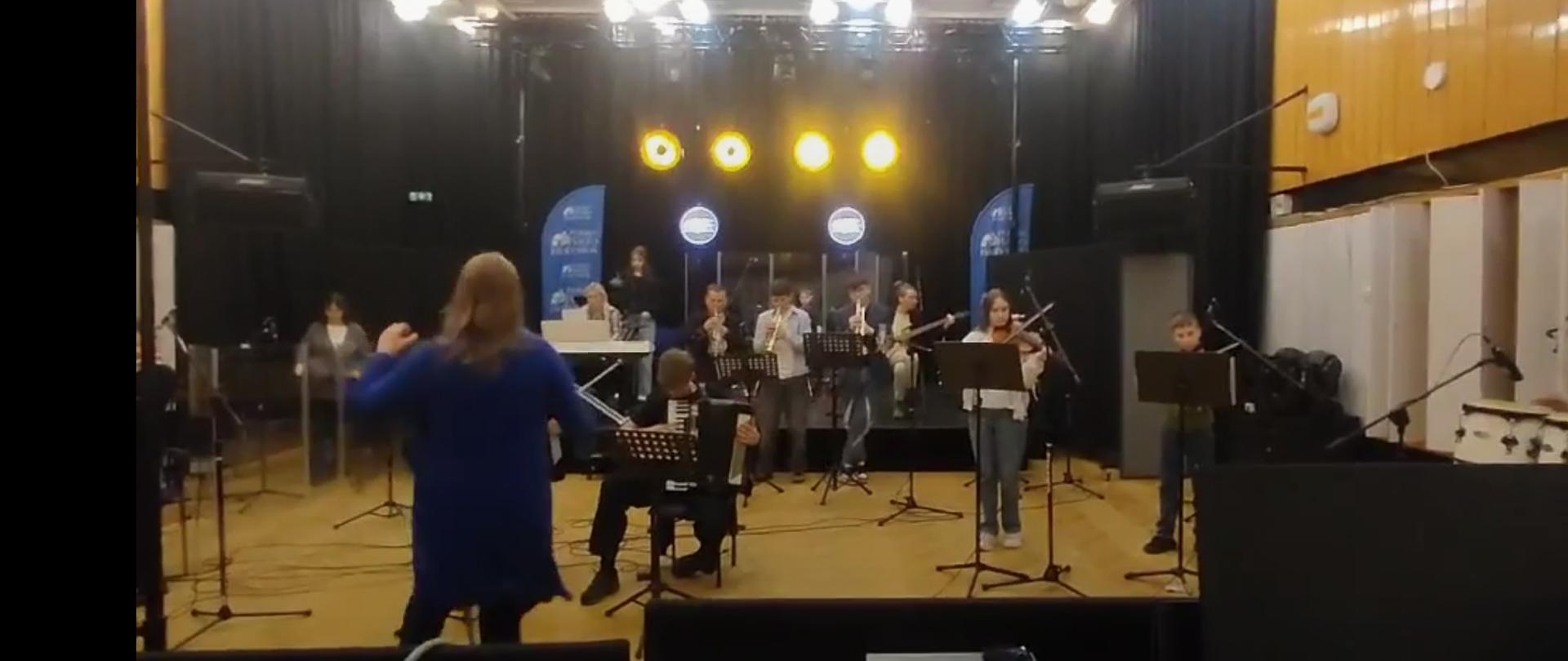 Widok z reżyserki na salę. Widzimy rozstawiony go gry zespół i dużo mikrofonów. W końcu jesteśmy w studio nagraniowym.